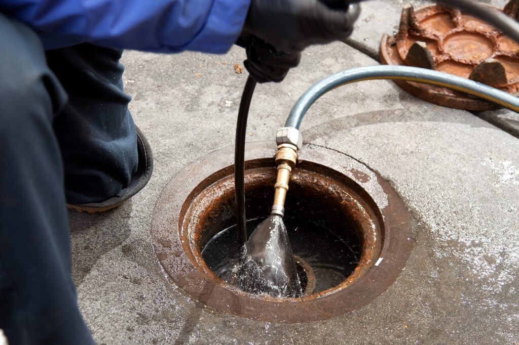 Plumber hydro jetting a sewer line through a manhole in Parker